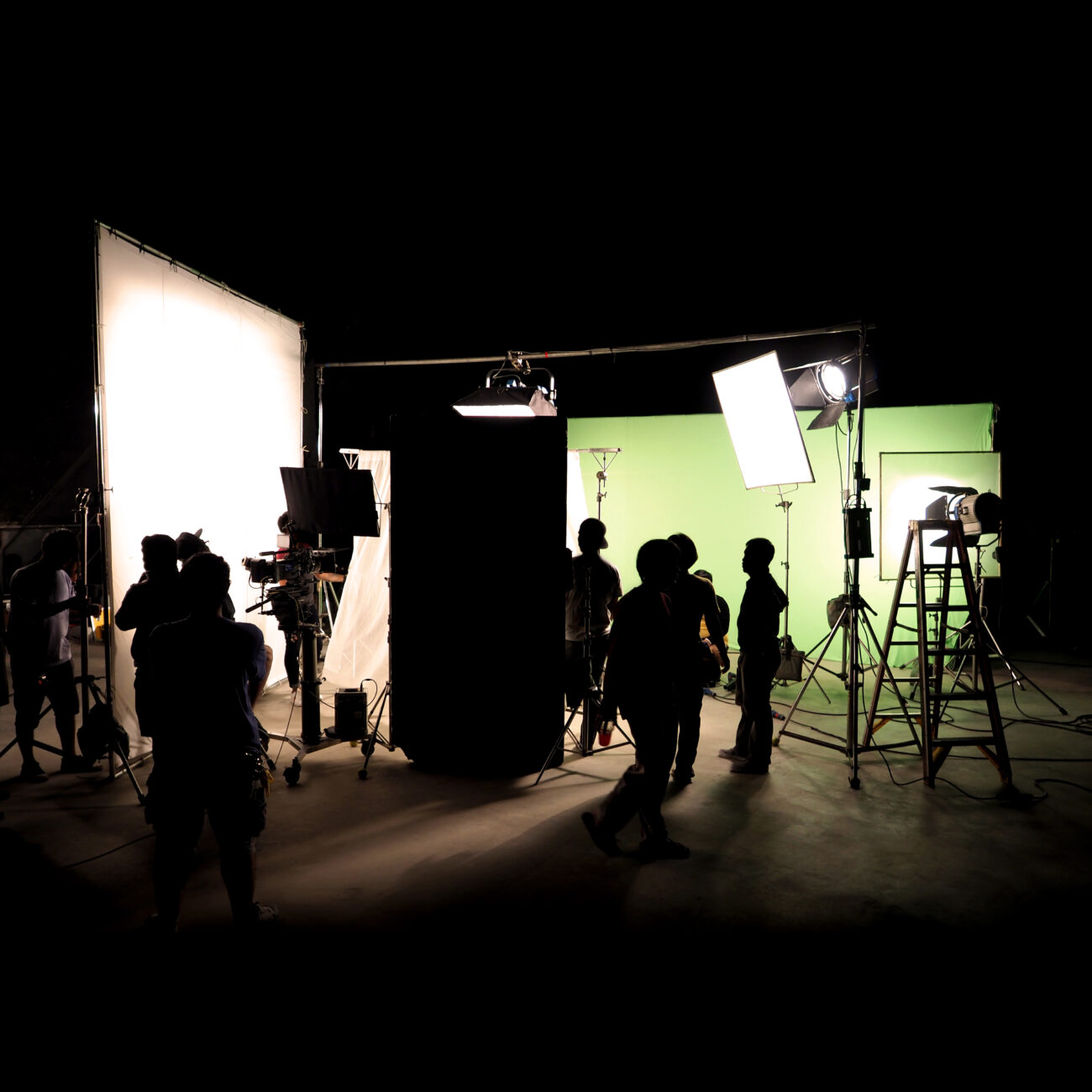 Silhouette images of video production behind the scenes or b-roll or making of TV commercial movie that film crew team lightman and cameraman working together with director in big studio with professional equipments